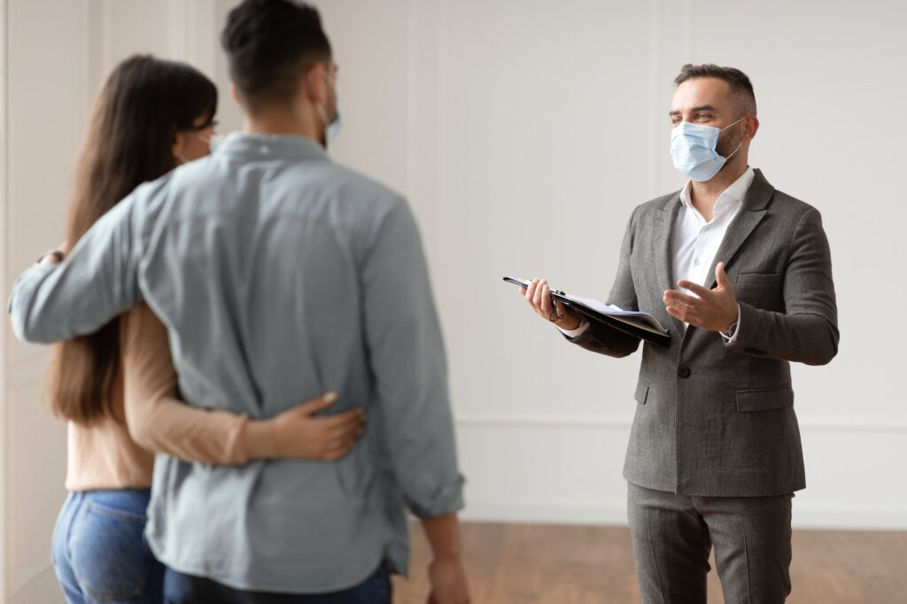 Male Realtor In Medical Mask Showing Buyers New Apartment