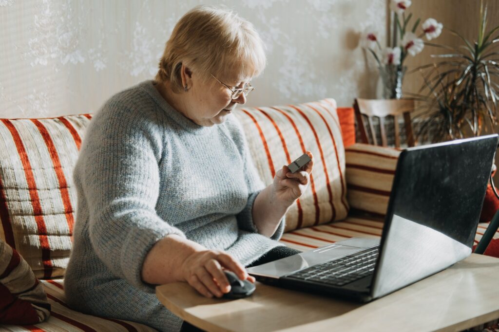 Senior woman Holding Credit Card near laptop at home. Mature woman shopping online, using credit